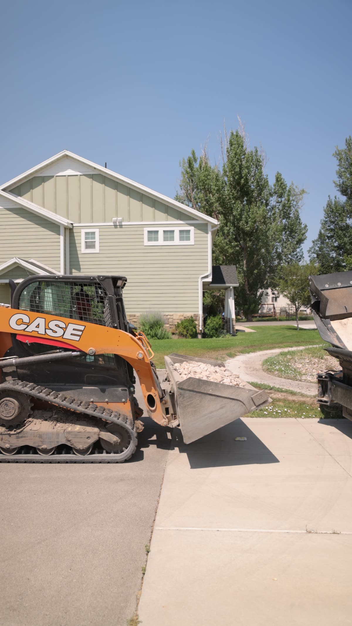 A skid steer feeding the conveyor hopper on a residential street
